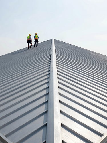 Low-angle architectural shot of a sharp standing-seam metal roof installation under bright, crisp daylight, safety-gear crew visible on the ridge