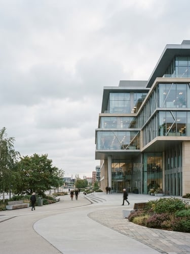 Wide-angle architectural film photography of a modern corporate headquarters building, clean symmetrical lines, soft natural overcast light, desaturated cool tones with warm sand accents, 35mm wide-angle, the building fills the right third of the frame, expansive sky.
