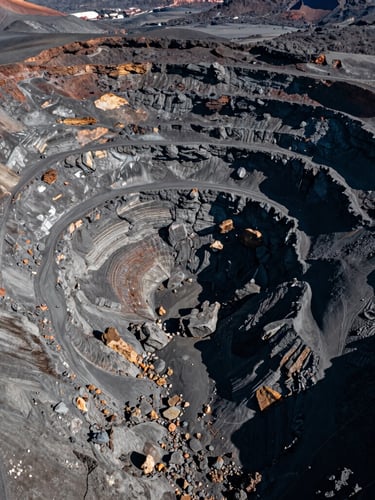 Aerial drone shot of a vast volcanic quarry landscape, deep basalt grays, harsh natural sunlight, sharp high-contrast details, 35mm