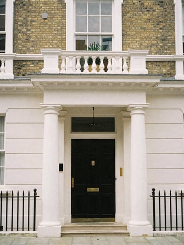 A straight-on architectural shot of a classic Chelsea townhouse with white stucco pillars under soft overcast London daylight, 35mm lens