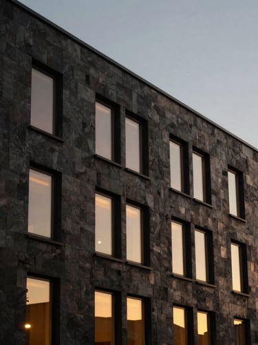 Low-key moody architectural shot of a modern building exterior in Somerset at dusk, warm golden light spilling from windows, sharp focus