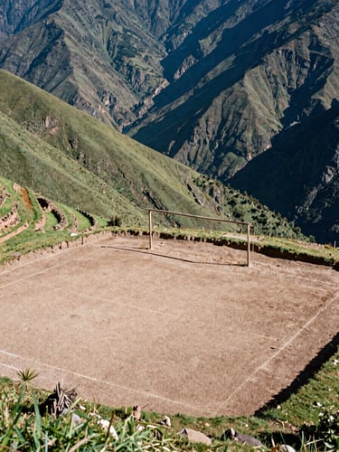 Wide-angle documentary shot of a newly terraced dirt soccer pitch carved into a steep green mountain ridge in Peru, natural harsh afternoon sun, a single rustic wooden goalpost, dramatic deep valleys in the background, 35mm film texture.