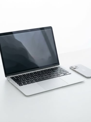 Sleek modern silver laptop and minimalist smartphone on a pristine white desk, bright high-key studio lighting, soft shadows, sharp focus, tech-retail aesthetic