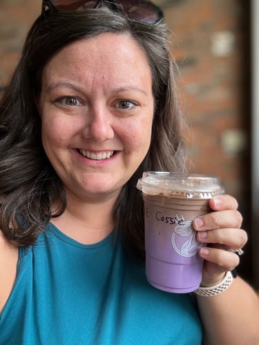 A smiling woman holding a cup of purple coffee