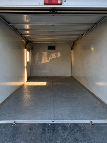 Wide-angle interior shot of the 14-foot garage cargo space in the Wolfpack trailer, clean grey coin flooring, heavy-duty steel tie-down rings flush in the deck, natural daylight pouring in from the open ramp door.