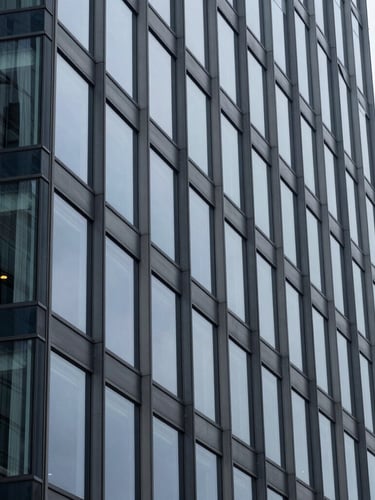 Close-up architectural detail of a modern glass office building facade, sharp geometric lines, cool overcast daylight, navy and slate gray tones