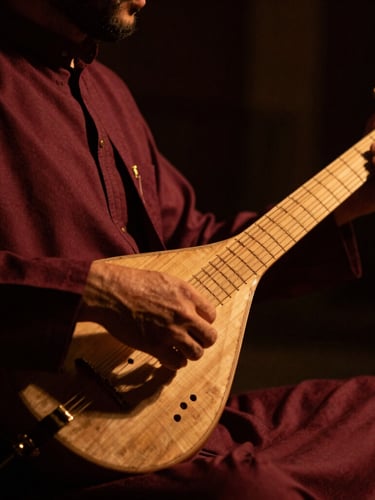 Dramatic close-up of a Sufi musician playing a traditional string instrument under low-key warm stage lighting, rich shadows, shallow depth of field