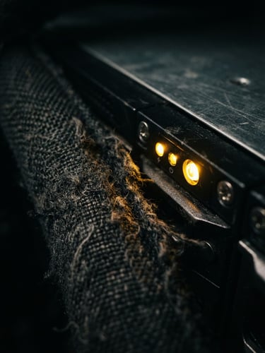 Moody close-up of dark textile fibers juxtaposed with glowing gold indicator lights of a server rack, sharp focus, dramatic studio lighting
