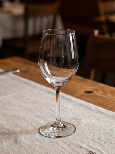 A close-up, side-lit shot of a rustic, Scandinavian-style restaurant dining table, an empty wine glass casting soft shadows on a linen tablecloth, warm wooden tones.