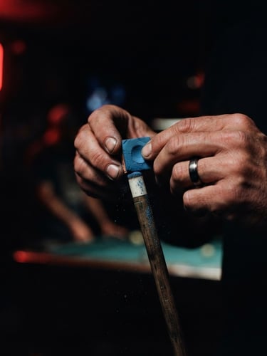Moody low-key close-up of hands chalking a pool cue under low red neon light, dark background, cinematic 35mm photography
