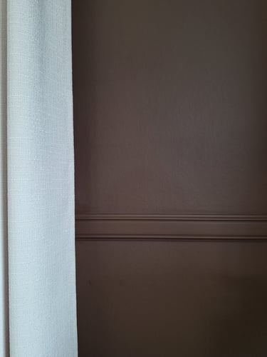 Zoom sur un mur brun avec une moulure et une tenture en lin beige