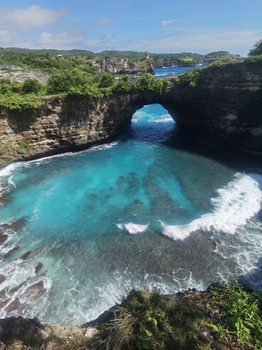 Scenic view of Broken Beach in Nusa Penida, Bali, featuring a natural limestone arch over turquoise ocean water.