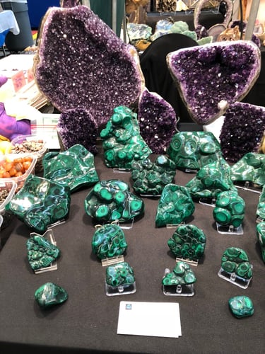 Polished green malachite stones and amethyst specimens displayed at a gem and mineral show.