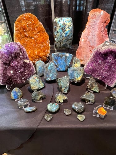 Collection of polished labradorite crystals and purple amethyst geodes displayed on a black table.