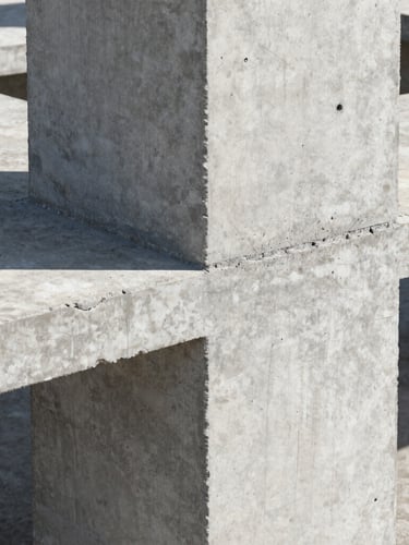 Crisp architectural close-up of a freshly poured concrete column joint with exposed steel reinforcement, harsh directional sunlight highlighting the heavy industrial texture.