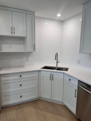 Corner sink area with white shaker kitchen cabinets, quartz countertop, subway tile backsplash, and