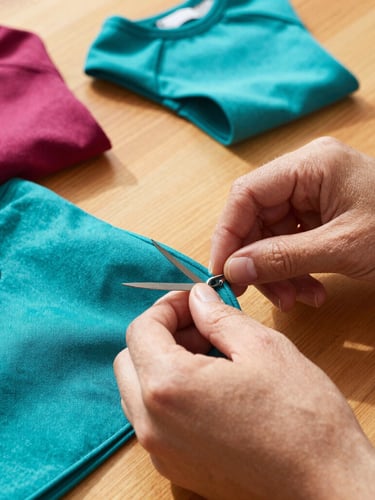 Hands of a Mexican artisan carefully cutting colorful fabric on a wooden table, warm sunlight, sewing patterns and pet clothes in the background, close-up, 35mm