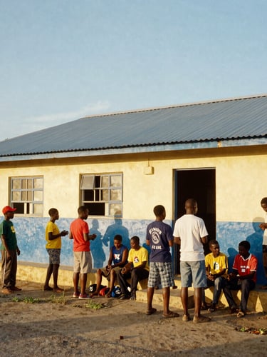 Wide environmental shot of Jamaican community members and Kiwanis volunteers collaborating outside a brightly painted schoolhouse in Oracabessa, warm golden hour sunlight.