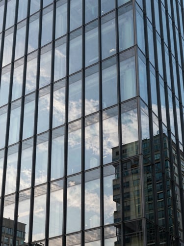 Crisp, daylight architectural view of a modern corporate glass facade reflecting a clear sky, symbolizing structured security and corporate-aligned risk mitigation.