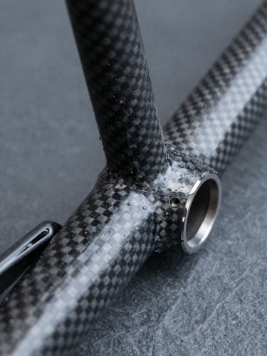 Macro detail of a high-performance carbon fiber bicycle frame joint, cool studio lighting, sharp technical photography, slate tones, depth of field.