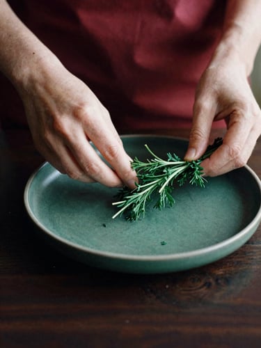 Hands styling a minimalist Scandinavian dish with fresh herbs under soft natural side-light, high-contrast matte finish, 35mm film