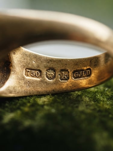 Macro close-up of vintage gold jewelry hallmarks, showing intricate stamps on a gold ring under soft natural window light with a shallow depth of field.