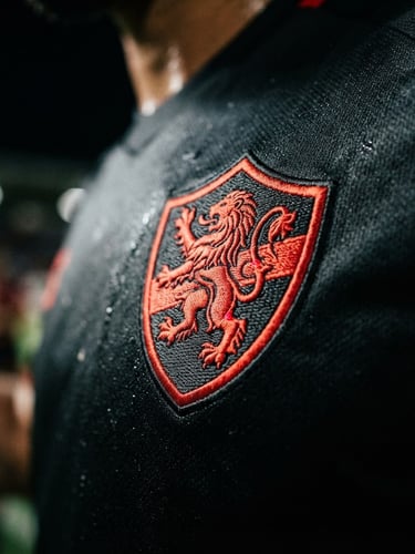 Dynamic close-up of a modern football jersey crest, sharp embroidery texture, dramatic stadium floodlights, high-contrast athletic photography, 35mm