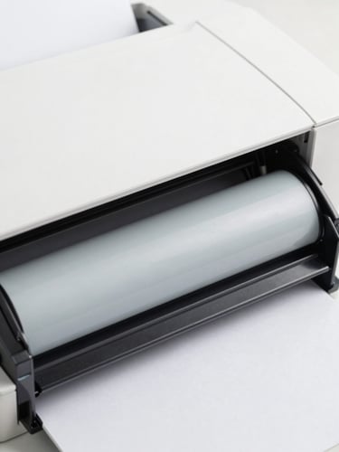 Macro close-up of a clean printer's internal mechanism, specifically a toner cartridge or paper feed roller, under bright studio lighting, sharp focus, minimalist white and light gray tones.