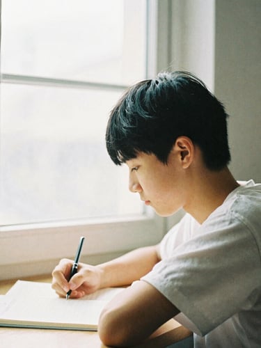 A quiet, high-contrast portrait of a young student studying by soft window light, warm editorial tones, shallow depth of field, 35mm film grain