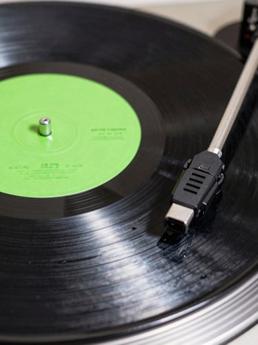 Extreme close-up of a vinyl record with a neon green label spinning on a turntable, high exposure white light, sharp shadows