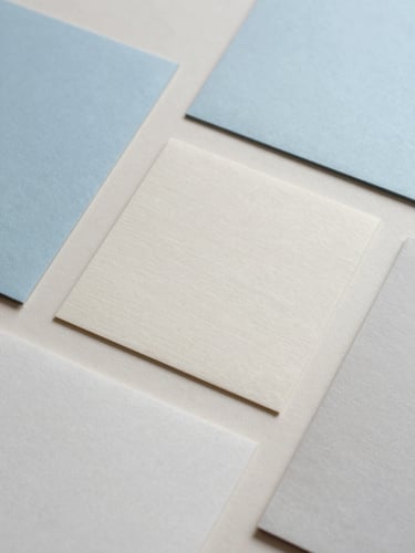A minimalist flat lay of tactile paper samples and soft shadows on a pale almond surface, overcast daylight, 35mm lens