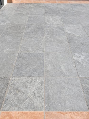 Straight-on architectural elevation of a modern outdoor terrace tiled with large-format slate gray tiles, showcasing flawless alignment and clean drainage integration, bright natural daylight, 35mm