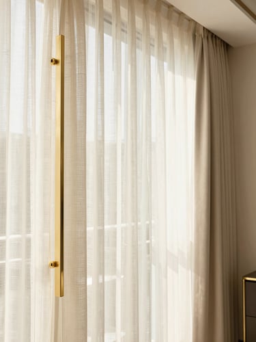 Straight-on architectural detail of premium champagne gold hardware holding sheer linen curtains, natural daylight flooding a warm beige corporate office, 35mm