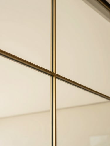Close-up architectural detail of a champagne gold partition joint on a floor-to-ceiling glass wall, soft natural light, warm beige background, minimal aesthetic