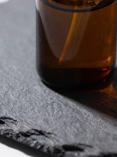 Macro close-up of a dark amber glass apothecary jar on a dark slate surface, crisp laboratory-style overhead light with sharp shadows, high contrast, sharp editorial product photography