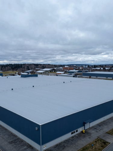 Architectural drone photography of a massive industrial flat roof with light grey PVC membrane, overcast Nordic daylight, deep blue and slate tones, crisp details, 35mm