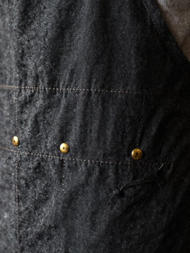 Close-up of a heavy charcoal canvas apron being stitched under warm side-light, brass rivets glinting, 35mm editorial textile photography