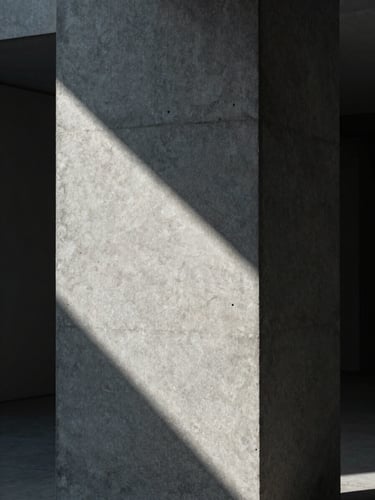 Portrait framing of a monolithic concrete column with sharp architectural shadows, cool diffused studio light, minimalist composition.
