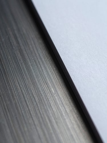 Extreme close-up macro shot of brushed metal intersecting with heavy matte paper, cool diffused studio lighting, sharp focus.