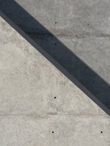 Extreme close-up of concrete architectural geometry, sharp diagonal shadow cast by hard midday sun, minimalist concrete wall texture.