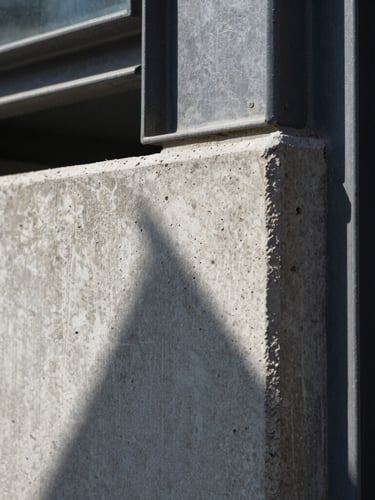Extreme close-up of raw concrete corner meeting a dark steel frame, sharp geometric shadow, hard direct sunlight, architectural detail
