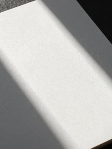 Portrait close-up of physical brand collateral, embossed white stationery on a heavy paper stock shot in sharp relief with hard, directional natural light casting geometric shadows.