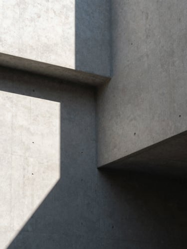 A high-contrast architectural corner with sharp, geometric concrete shadows cast by hard natural light, clean lines, minimalist composition.