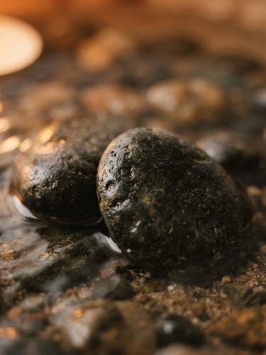 Macro close-up of smooth basalt stones resting in warm water, soft candlelit glow, muted earth tones, shallow depth of field, 35mm film