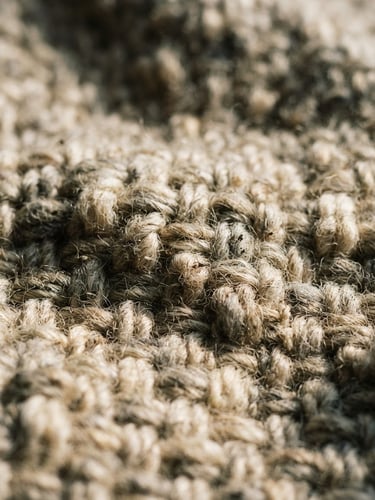 Macro photograph of heavy-gauge oatmeal wool weave, soft morning window light casting long shadows across the tactile threads, 35mm