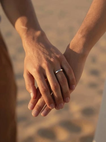 Portrait-oriented close frame of a couple's hands holding loosely, late afternoon light from the left, a ring catching a sliver of sun, warm terracotta and sand tones, shallow focus on the point of contact