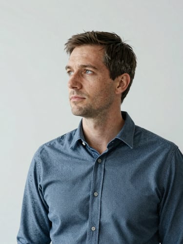 Portrait of a professional strategist looking thoughtfully sideways, soft natural studio light, desaturated technical tones, minimalist background, 35mm lens.
