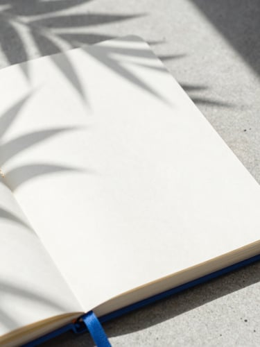 Extreme close-up of a high-end physical planning notebook on a concrete desk, sharp tropical shadows from window blinds, bright high-key lighting