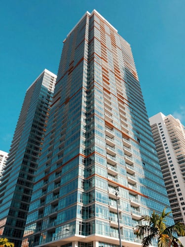 A portrait-oriented architectural photograph of modern glass skyscrapers in Brickell, Miami, shot from a low angle under intense, sharp tropical daylight with deep geometric shadows and a vivid blue sky, 35mm.