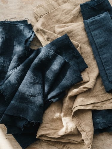 Overhead flat-lay of folded raw indigo cotton and warm sand linen swatches, soft morning daylight, high-contrast shadows, macro textile photography, 35mm